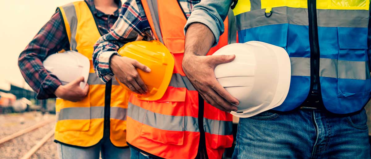 Industrial workers lined up holding their safety helmets at their waistline