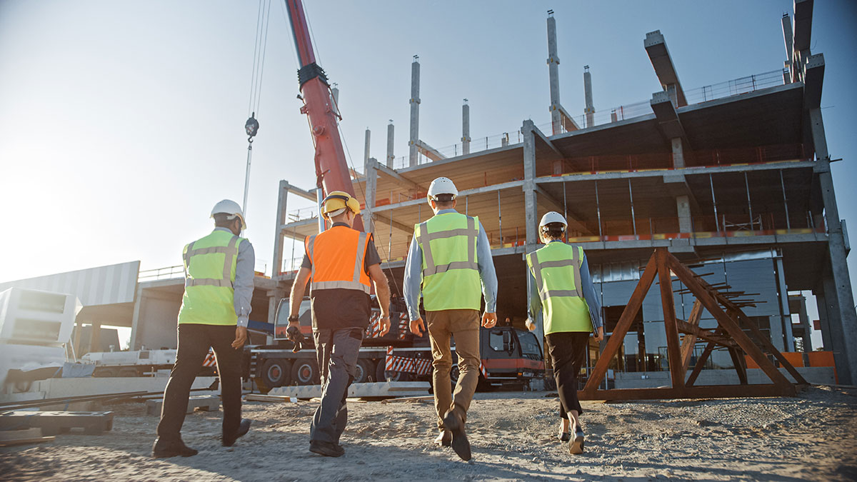 Diverse Team of Specialists Inspect Commercial, Industrial Building Construction Site. Real Estate Project with Civil Engineer, Investor and Worker. In the Background Crane, Skyscraper Formwork Frames