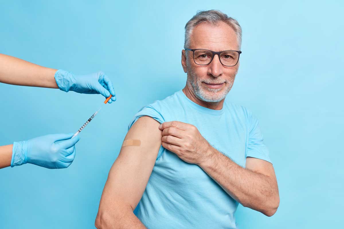 man pointing to a blue bandaid on his shoulder where he was given an immunization shot.