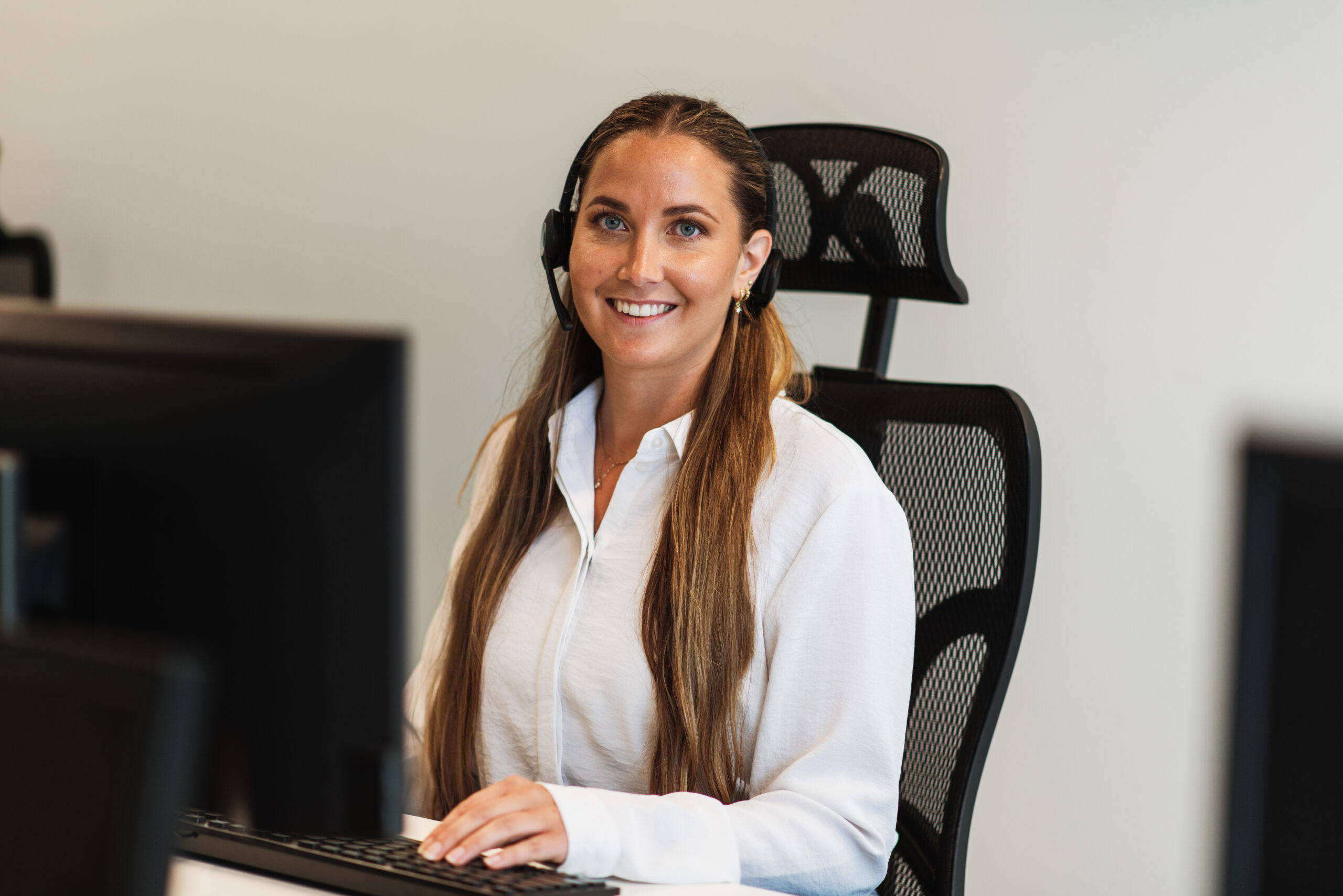 Smiling customer service representative wearing a headset at a modern office desk, reviewing a credit check on her computer screen.