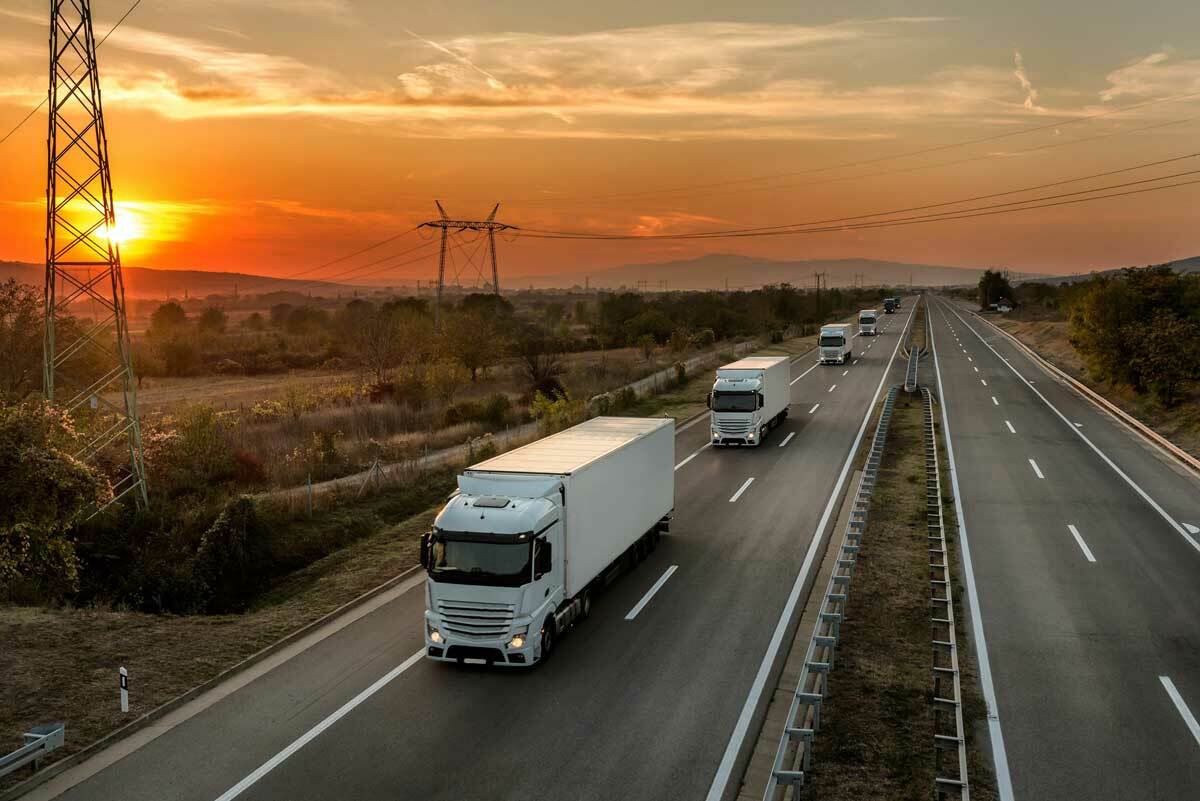 18-wheeler trucks driving in a line on the highway at sunset