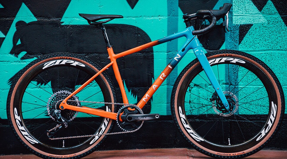 Photo of an orange and blue custom bike against a decorative wall