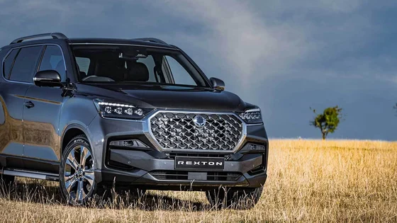 A KGM motors model vehicle parked in a dry grass field with blue sky in the background.
