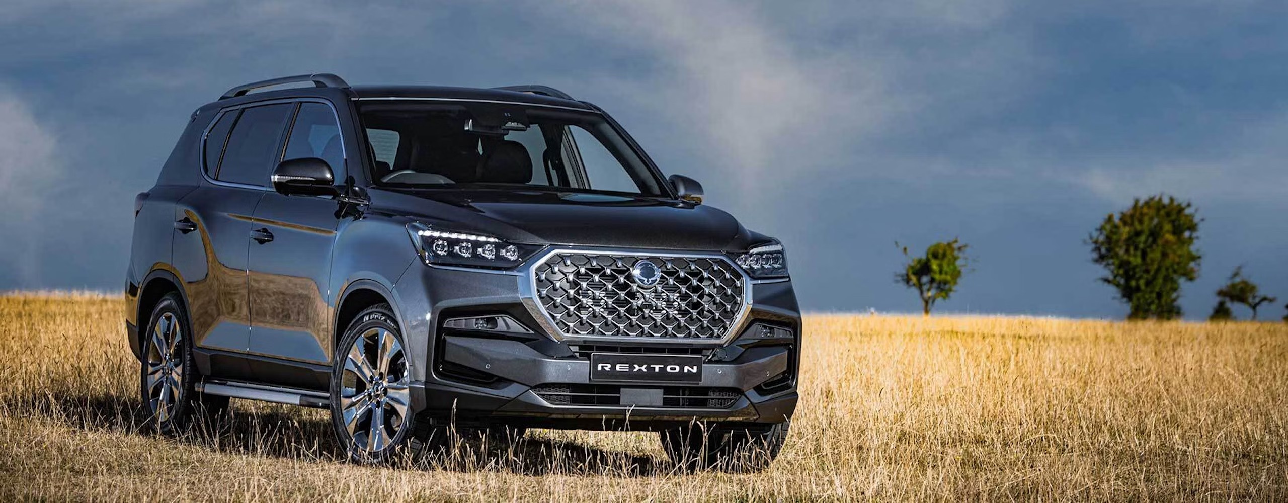 A KGM motors model vehicle parked in a dry grass field with blue sky in the background.