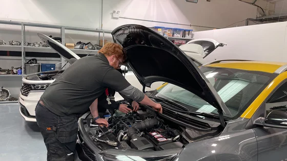 A motor Vehicle student looking into a cars bonnet to fix something