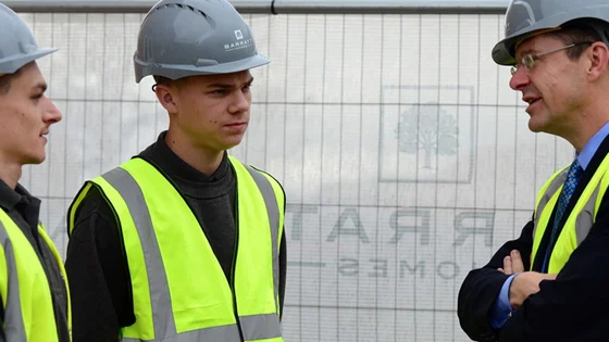 Two students in hard hats and hi vis talking to an employer on a construction site