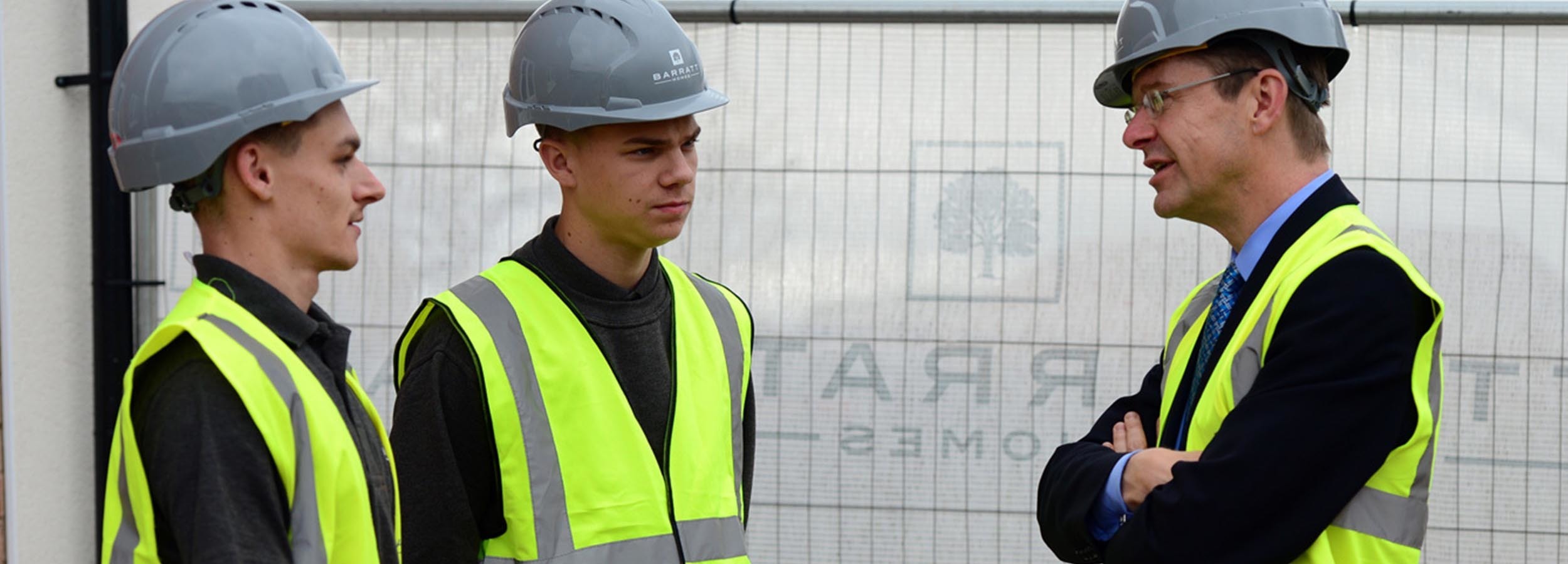 Two students in hard hats and hi vis talking to an employer on a construction site