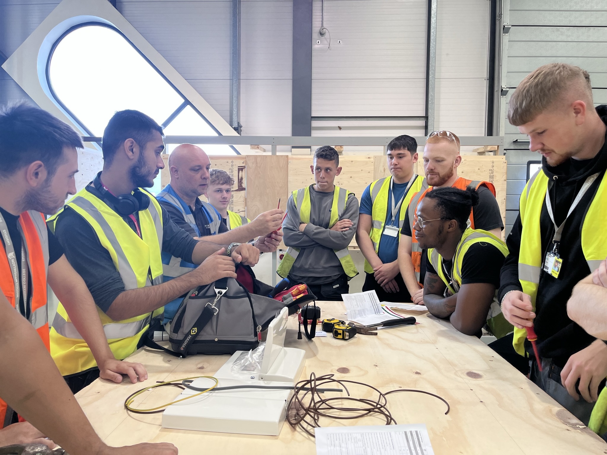 Apprentices gathered around a workbench listening to a lecturer talk