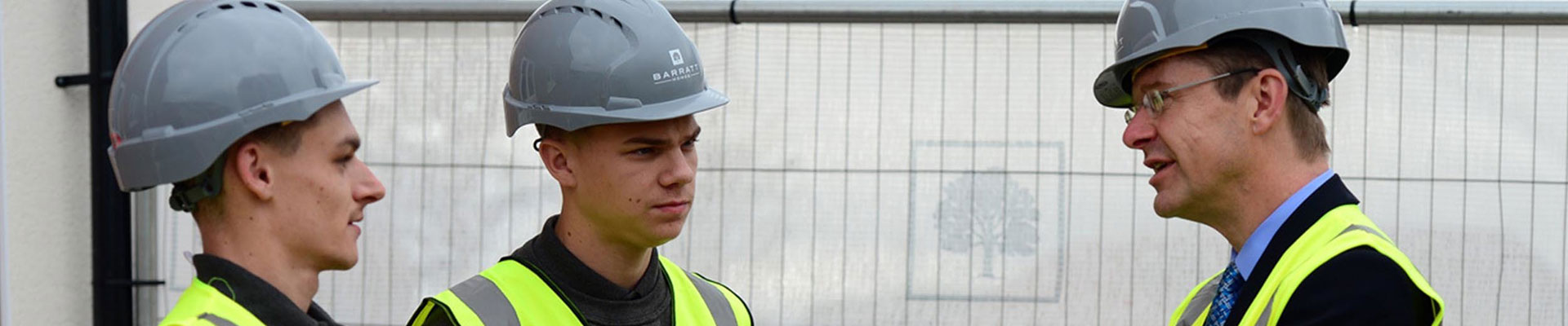 Two students in hard hats and hi vis talking to an employer on a construction site