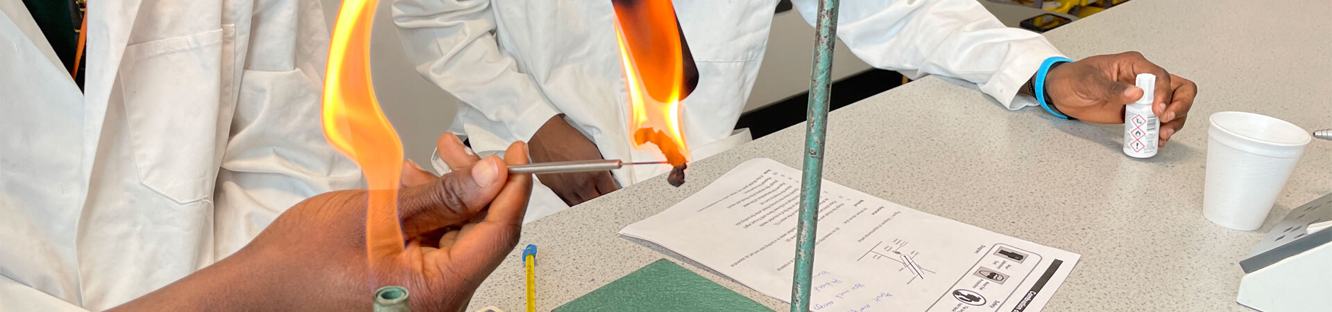 Two students working in a science lab using a Bunsen burner