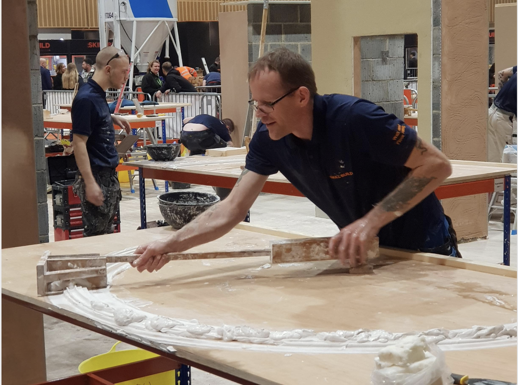 Mark plastering a piece of wood in a workshop