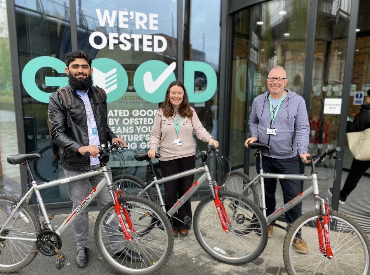 Three members of staff standing outside the City Hub holding bikes.