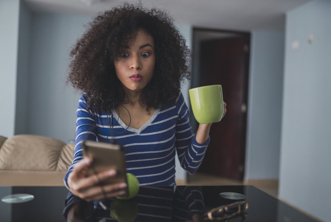 A female holding a phone in one hand with a surprised look on their face.