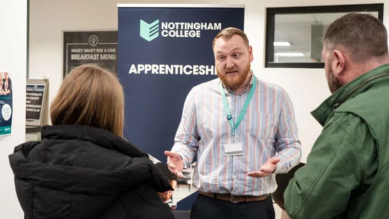 A member of staff talking to people about apprenticeships at an open event.