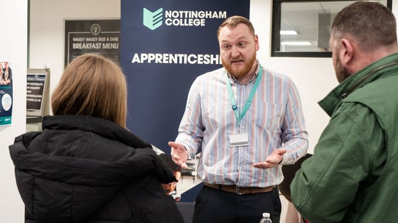 A member of staff talking to people about apprenticeships at an open event.