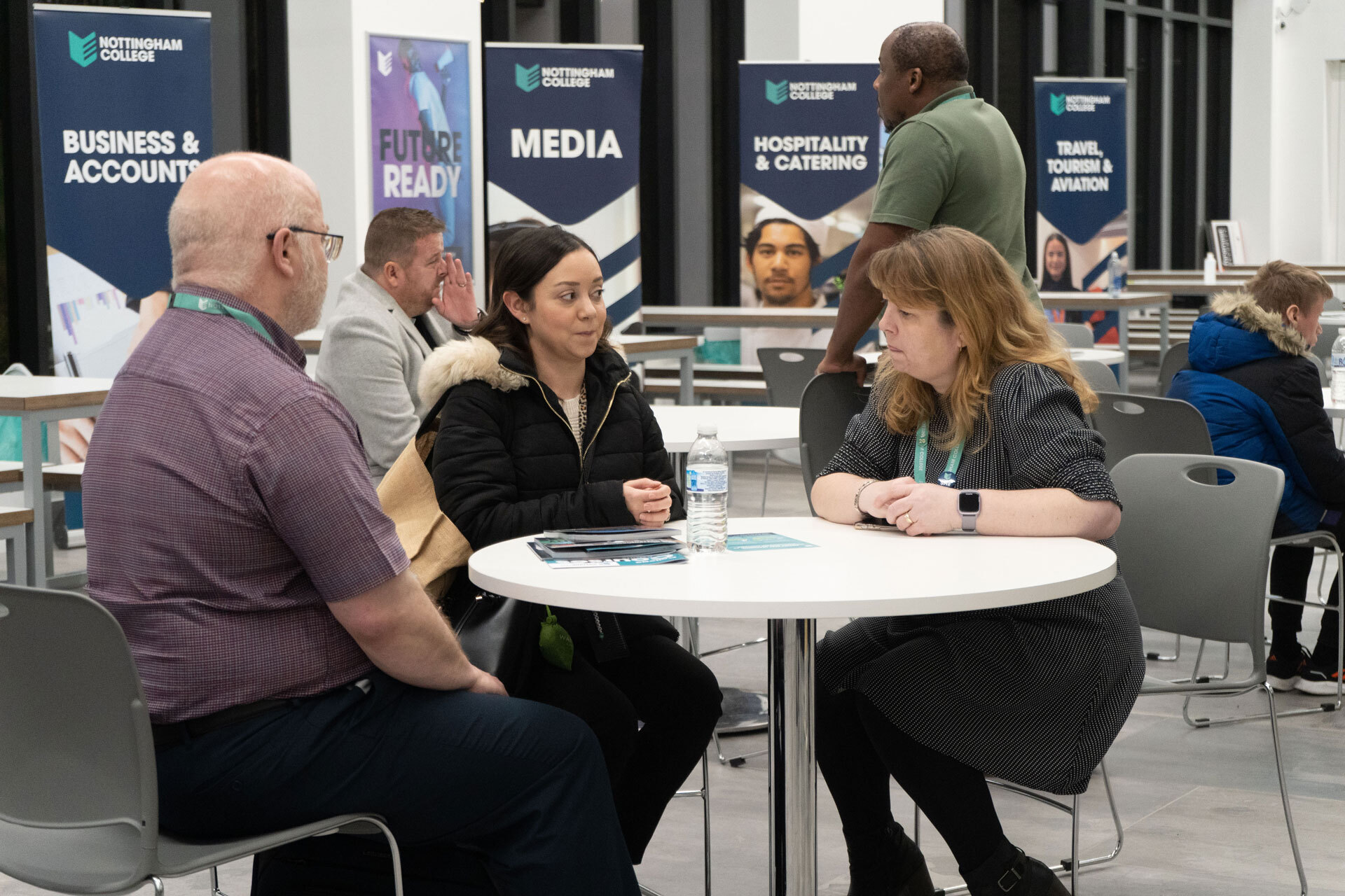 A student talking to two members of staff sat at a table during an open evening