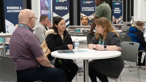 A student talking to two members of staff sat at a table during an open evening