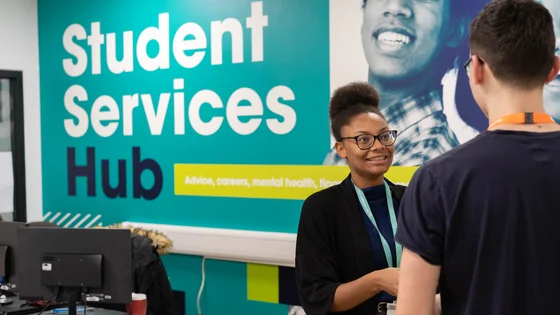 Member of staff with a student, smiling at our Student Services Hub