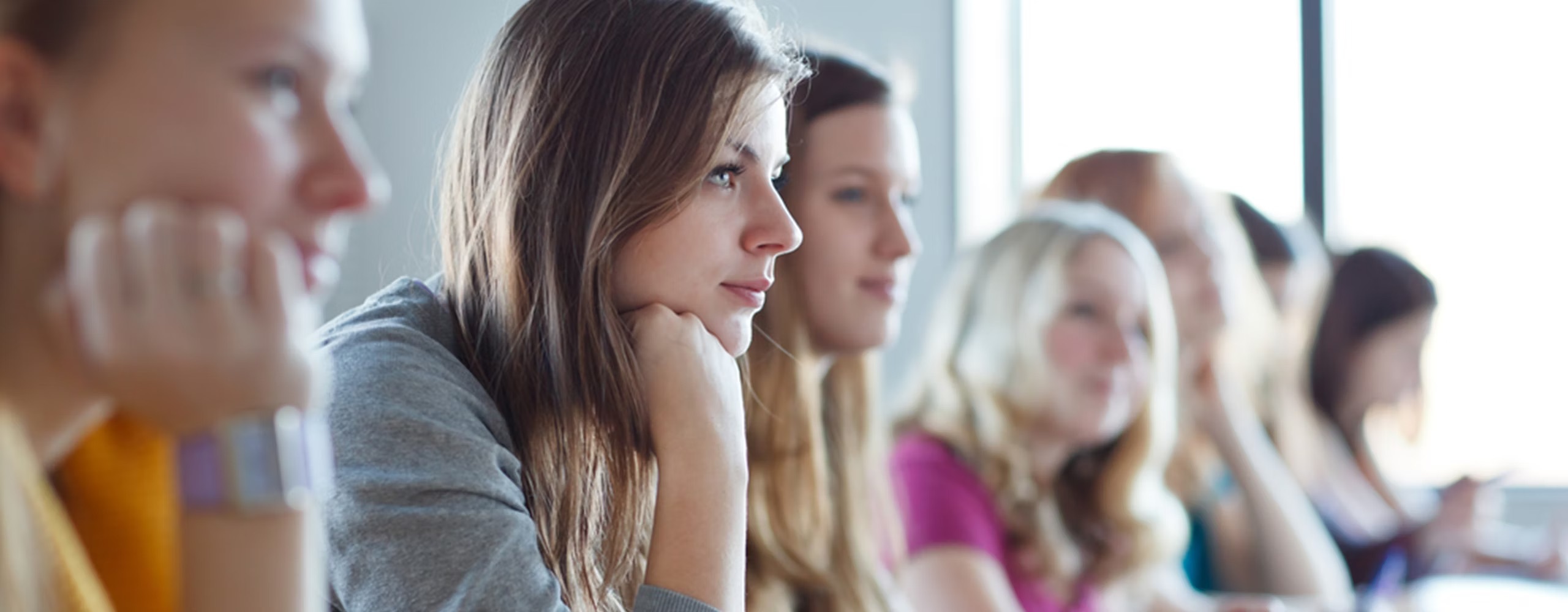 A row of students sitting at a desk in a classroom looking at the lecturer.
