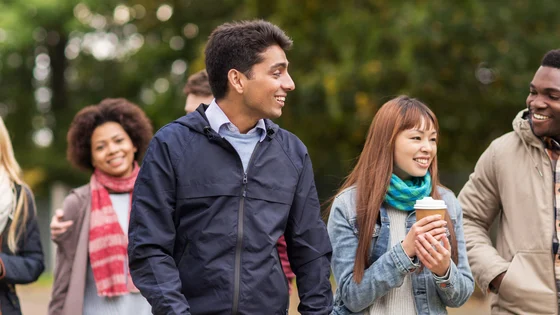 A group of young students walking in a park wearing scarves and carrying coffee.