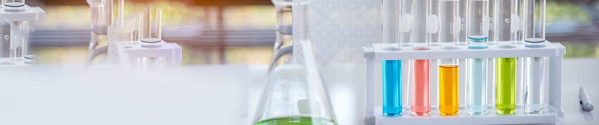 A conical flask and a rack of test tubes holding coloured liquid on a white desk.