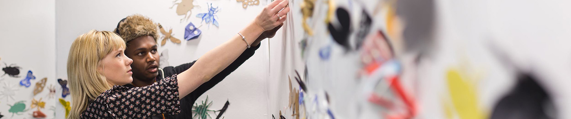 Students pinning artwork to an installation