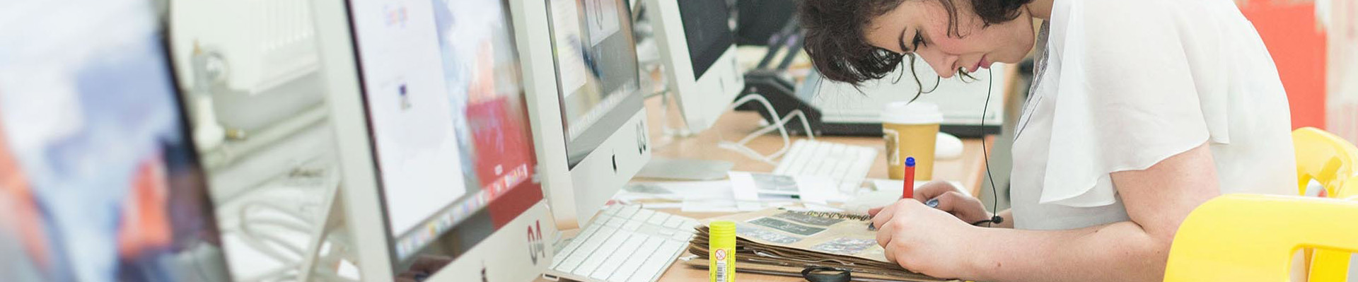A student sitting at a computer screen drawing with a pencil