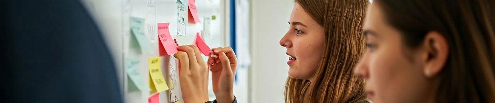 Two students sticking notes to a whiteboard during a business marketing lesson.