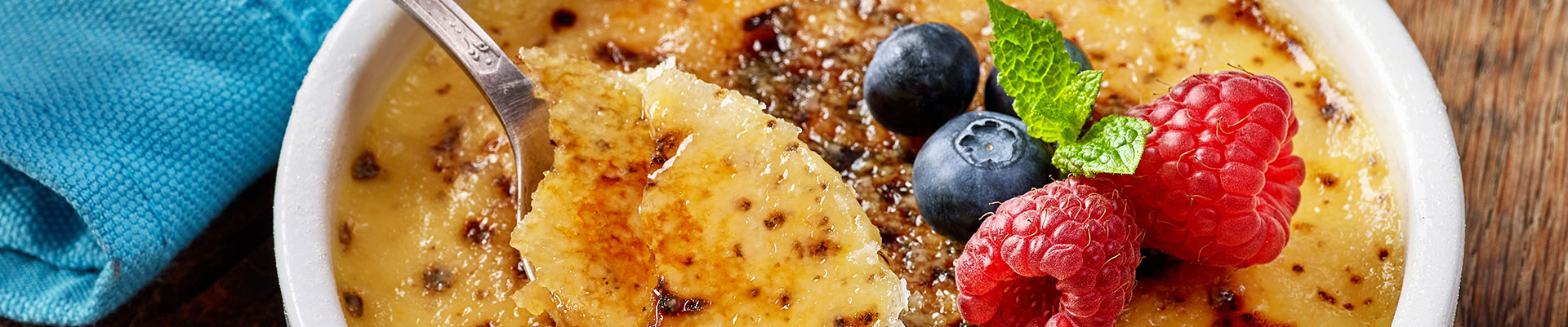 A bowl of homemade creme brulee with fresh berries on wooden table