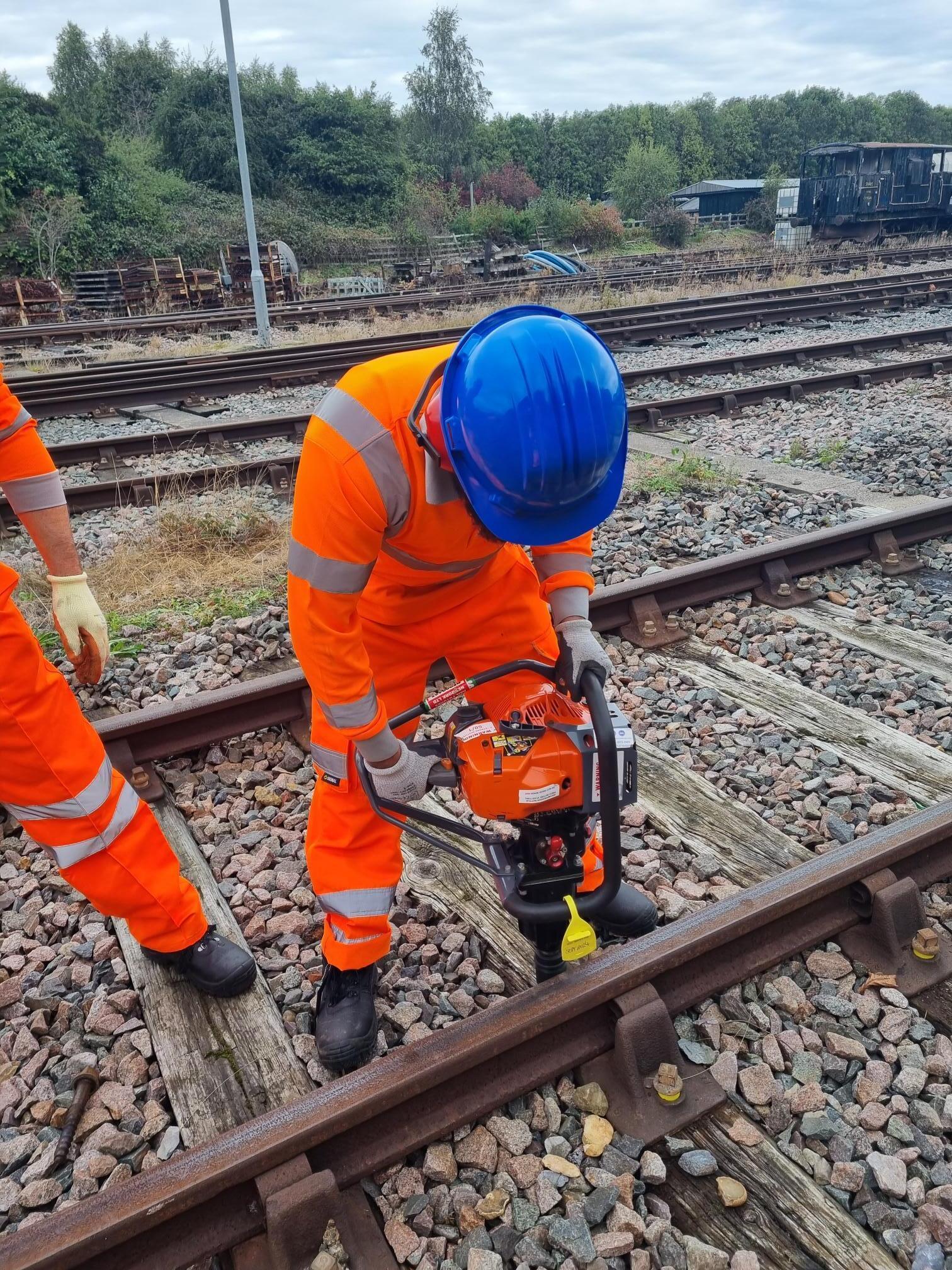 Rail workers using an impact wrench on a section of rail track.