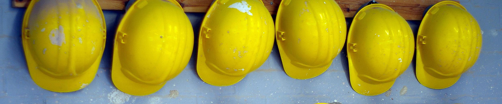 Six yellow hard hats hanging on hooks.