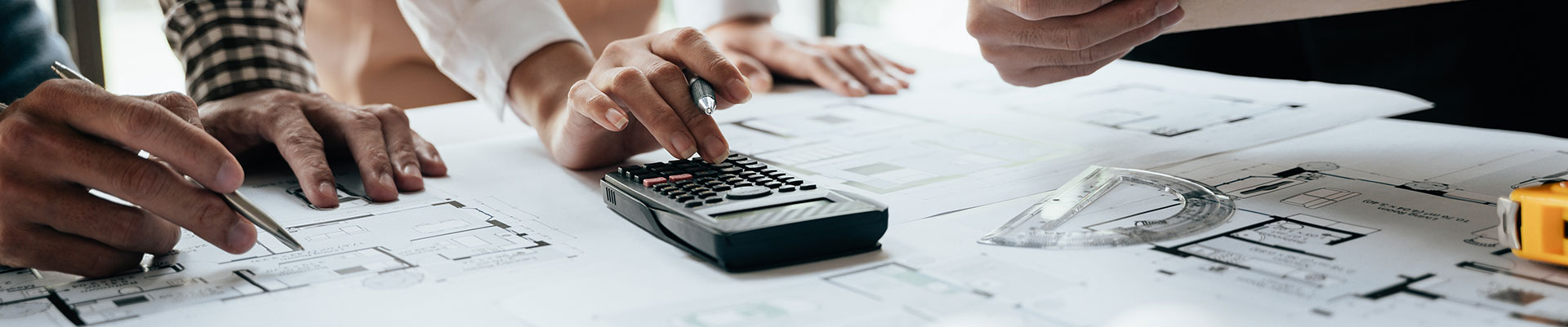 A group of students looking at architects' drawings, making notes and using a calculator.