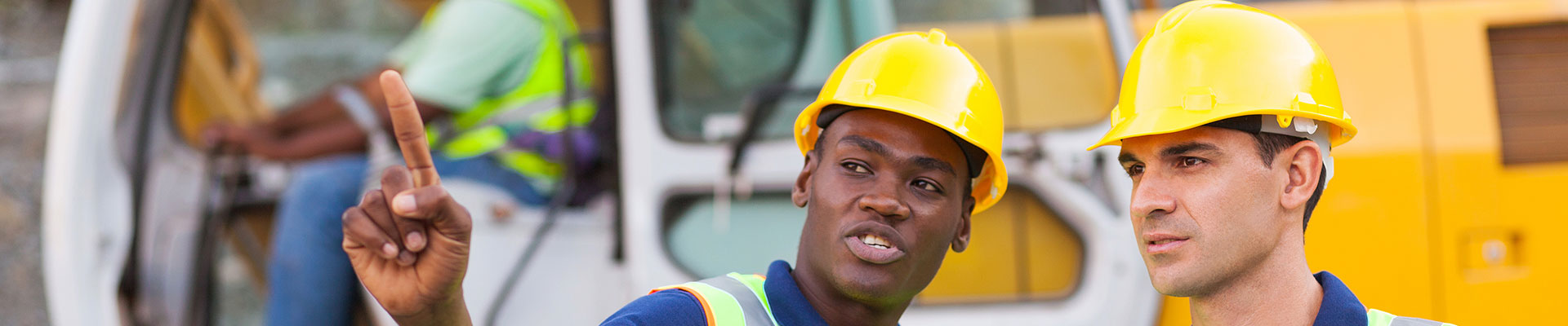 Two construction site workers talking in front of a mechanical digger.
