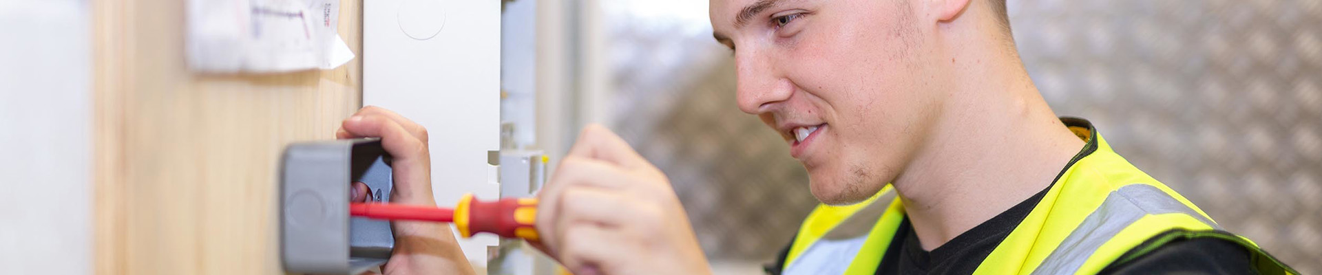 A student fixing an electrical socket to a wall.