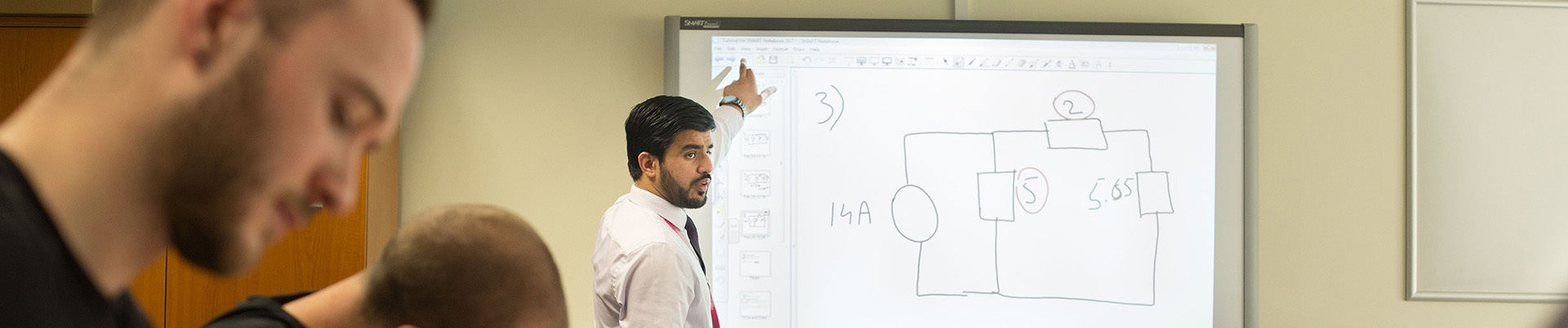 A lecturer teaching a class pointing at a smartboard