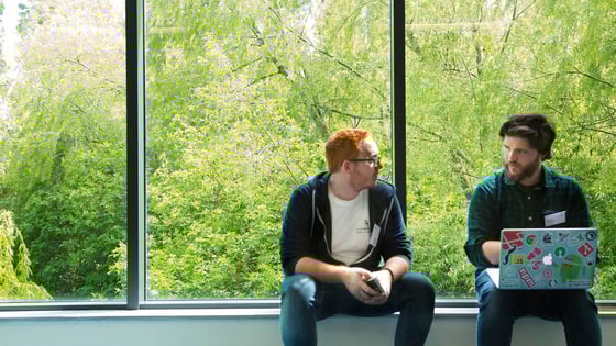 Two students sitting on a ledge, with a laptop with stickers