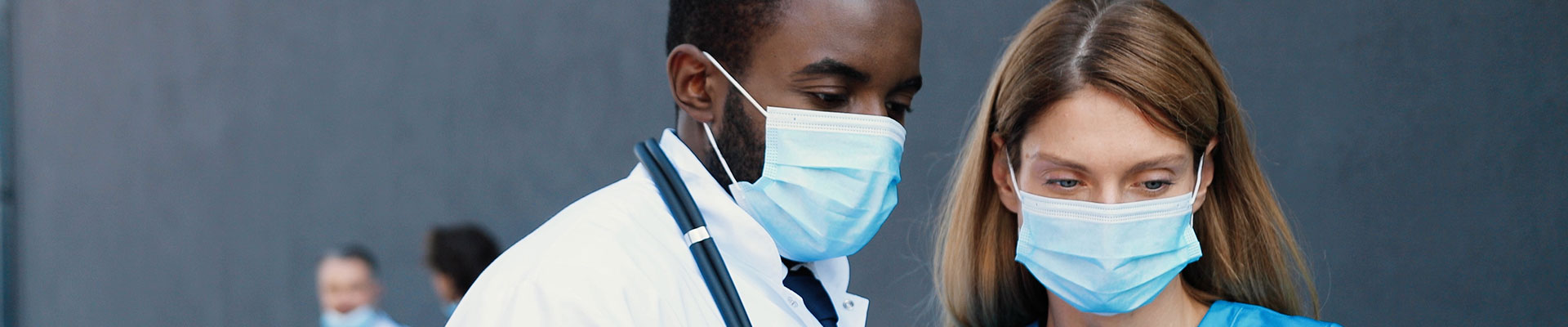 Two medical professionals wearing masks looking at a screen.