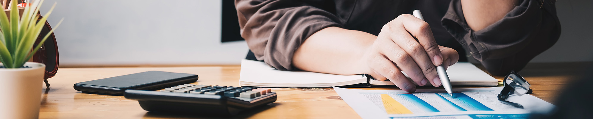 A student at a desk writing with a calculator and her phone.