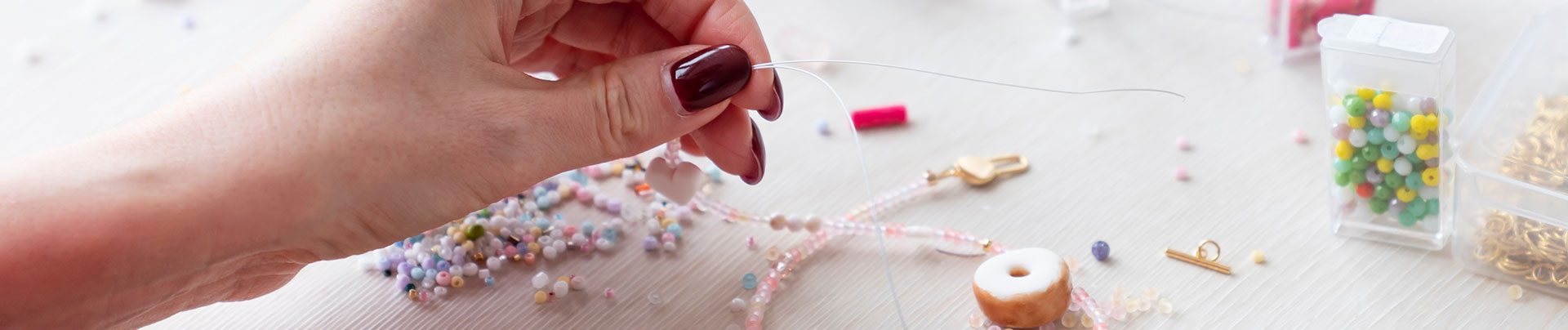 A person's hand making jewellery with beads.
