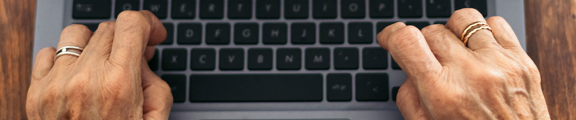 An older person's hand typing on a laptop
