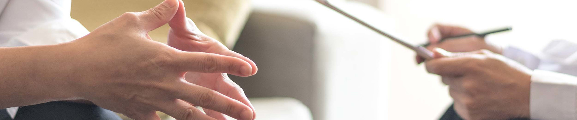 A sitting person talking a another who is writing notes on a clipboard.