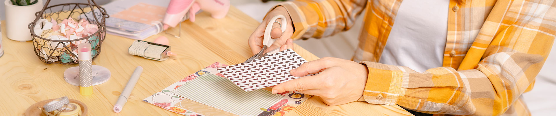 A person sitting at a desk cutting paper for scrapbooking.