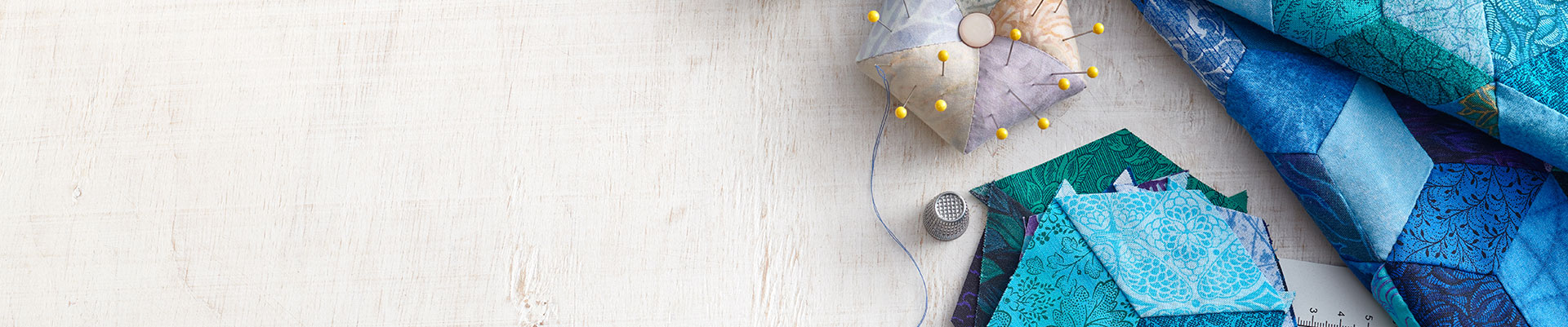 A pin cushion, thimble and a blue patchwork quilt.