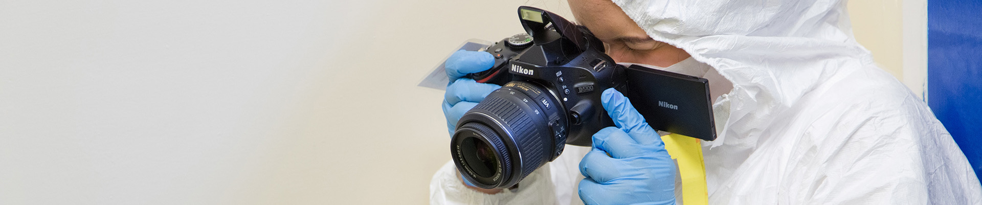 A forensic science student in protective clothing photographing evidence