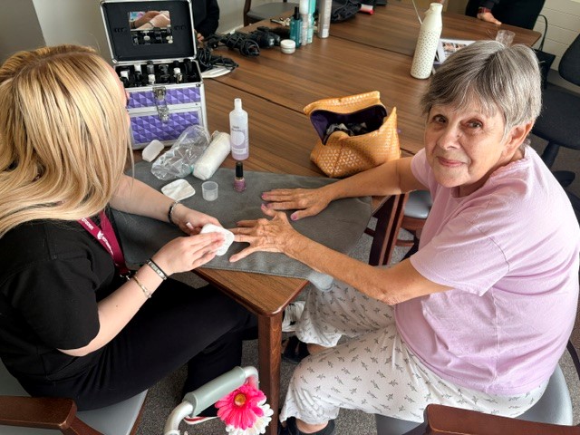 student painting nails of care home resident wo's smiling at the camera