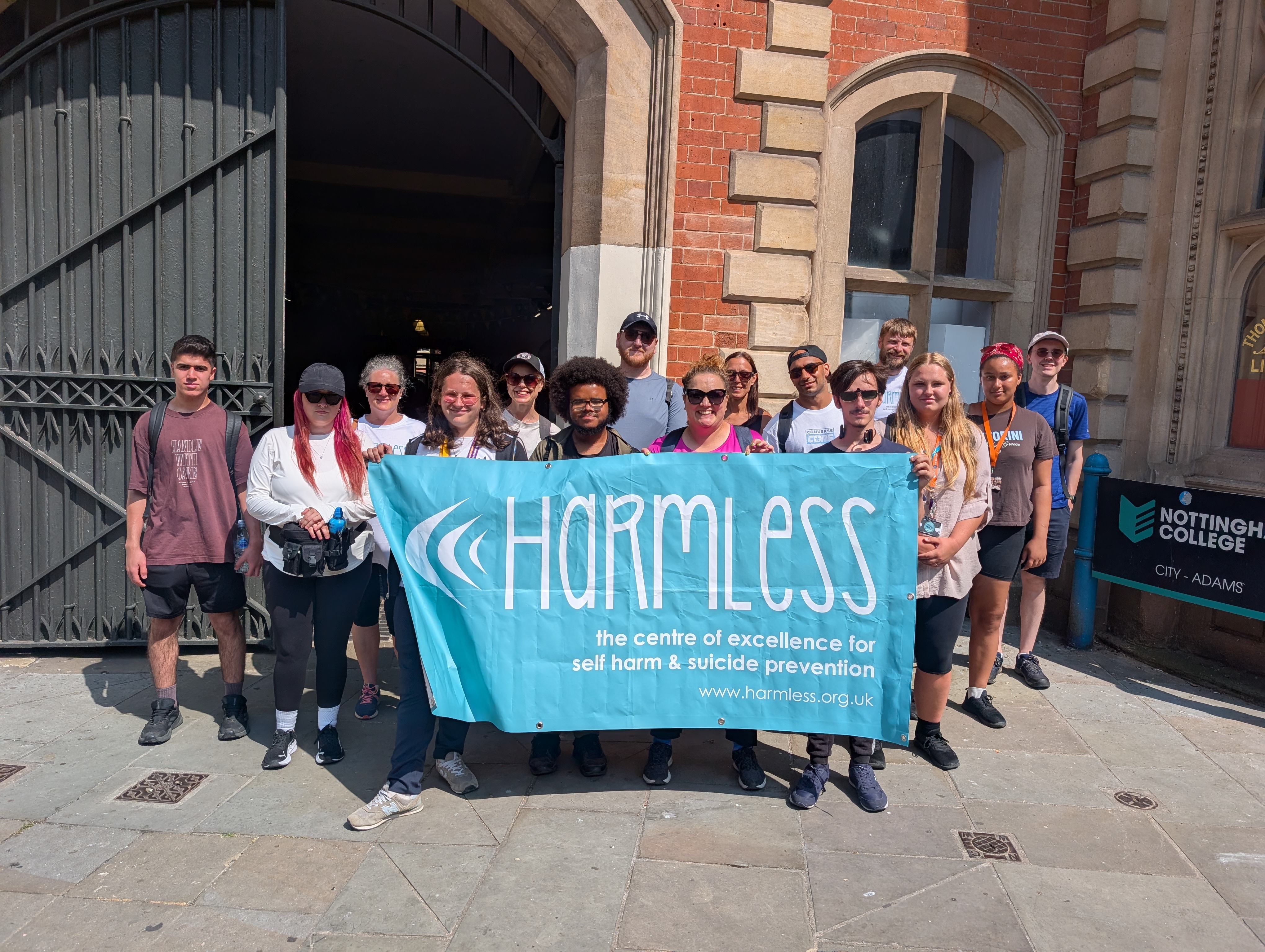 Staff and students outside Adams holding a banner that has the charity Harmless text written on it