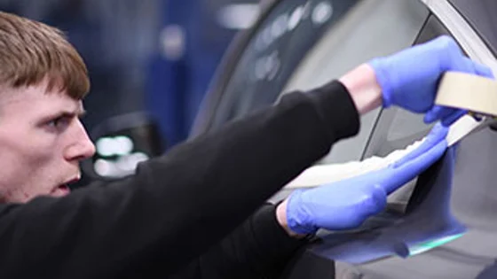 An apprenticeship apply masking tape to a car