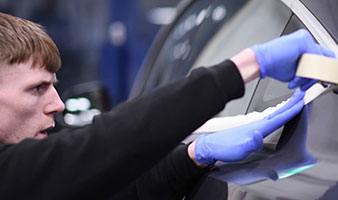 An apprenticeship apply masking tape to a car