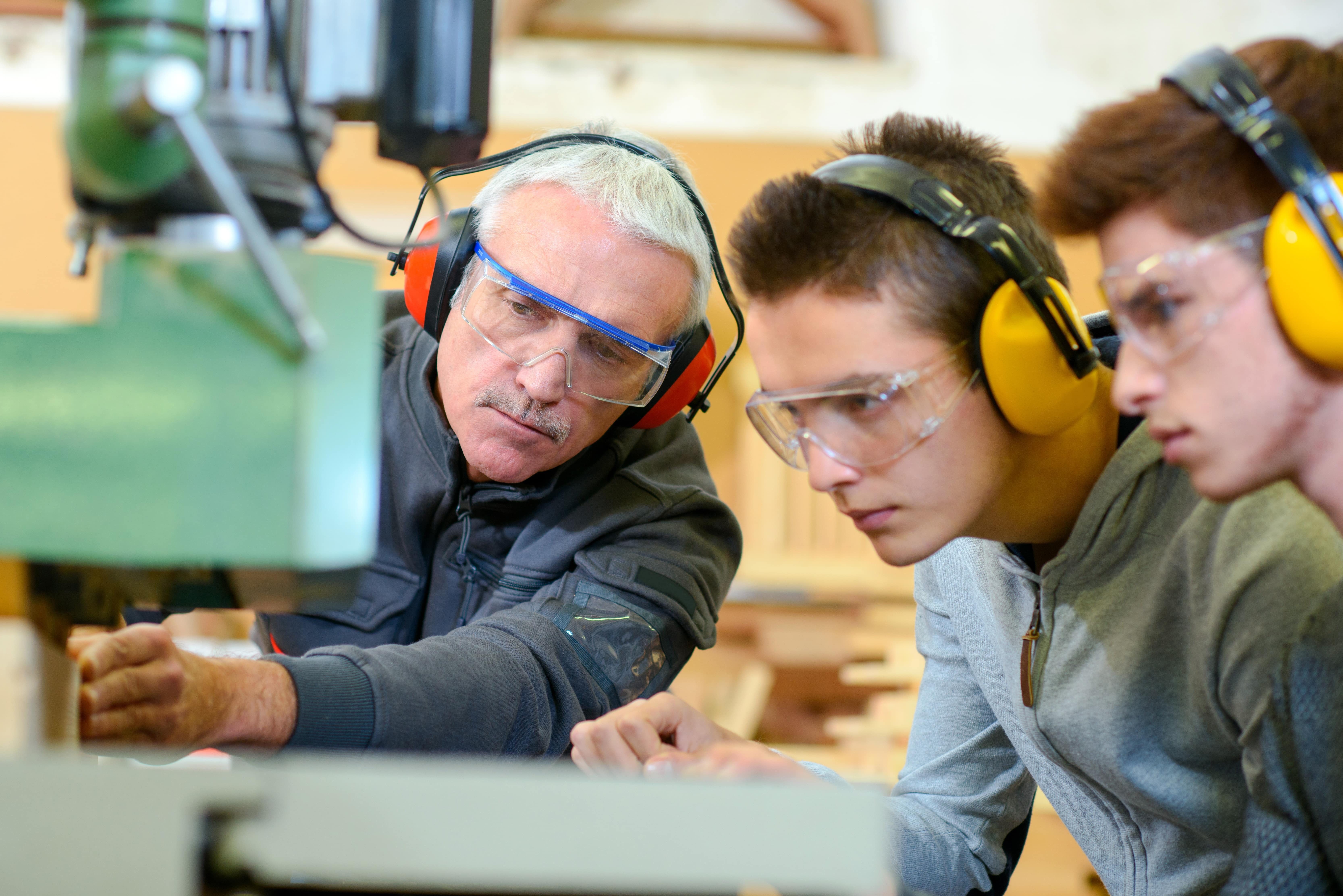 Two students observing a lecturer operating a machining drill.