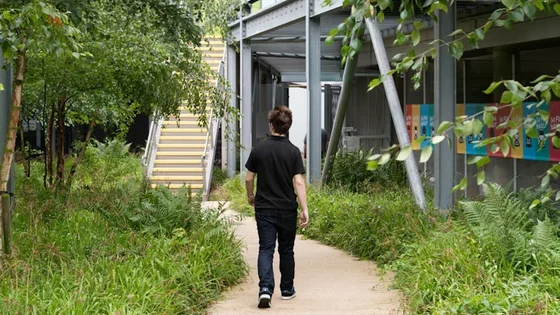A student walking towards the Highfields campus on a pathway with green grass and trees